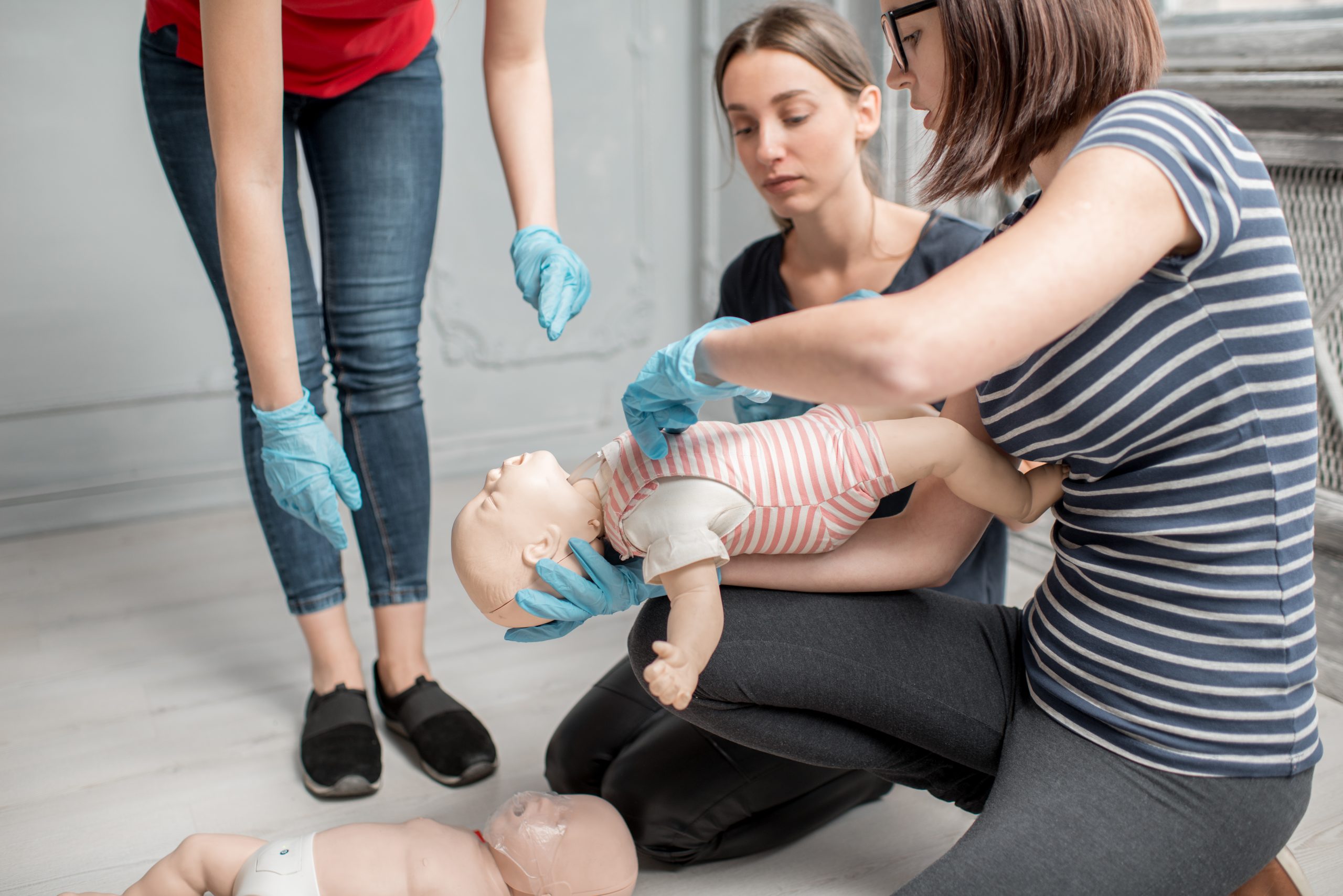 Woman learning how to make chest compressions on a baby dummy during the first aid group training indoors