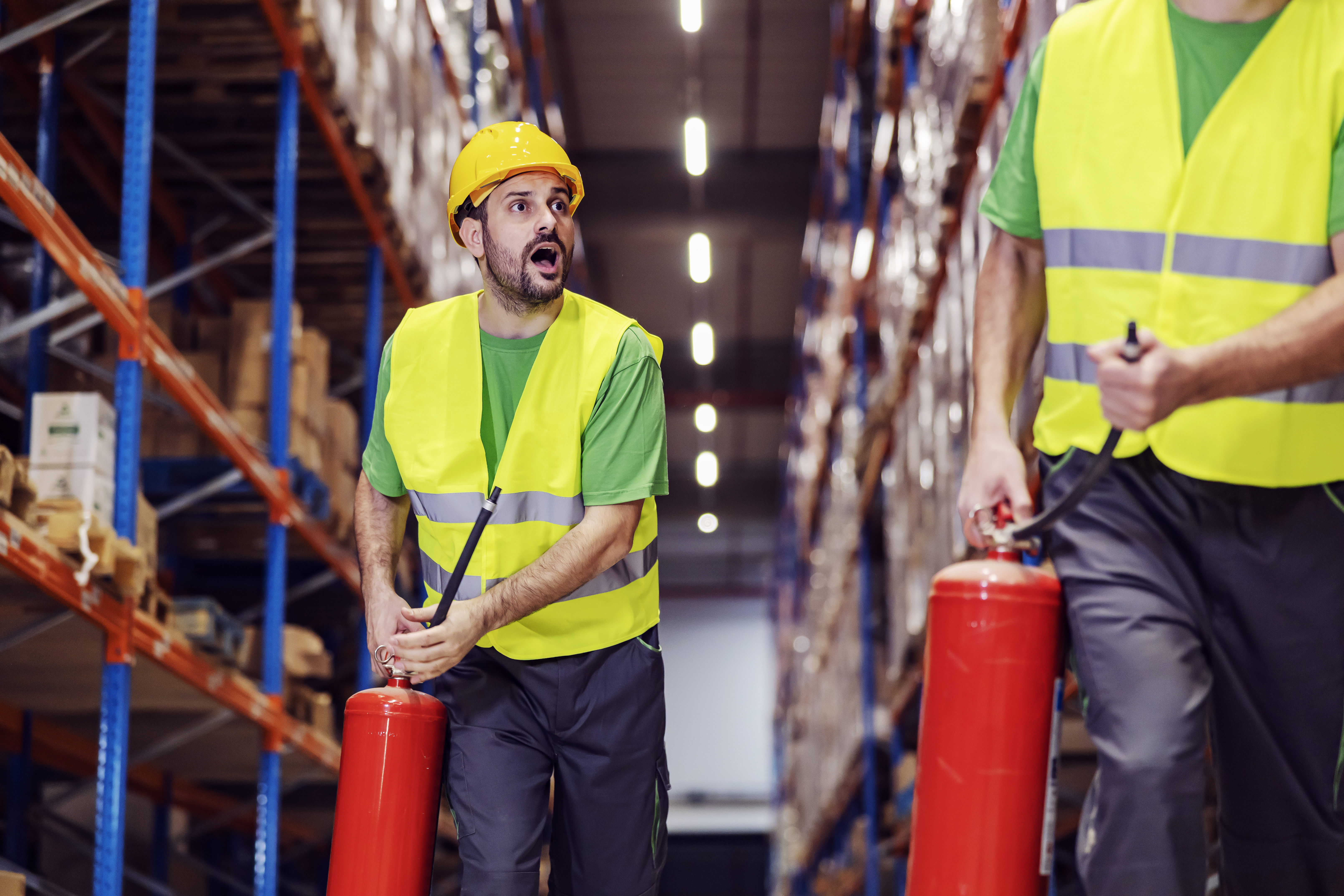 Panicked warehouse workers with fire extinguishers in hands rushing place of fire.