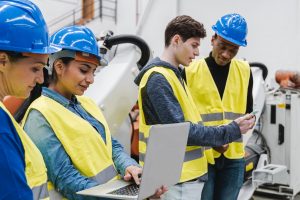 Multiracial industrial engineers working at automated AI robotic production factory – New technology concept